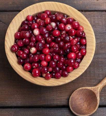 red berries of ripe lingonberries in a wooden bowl on a brown table, top viewの写真素材