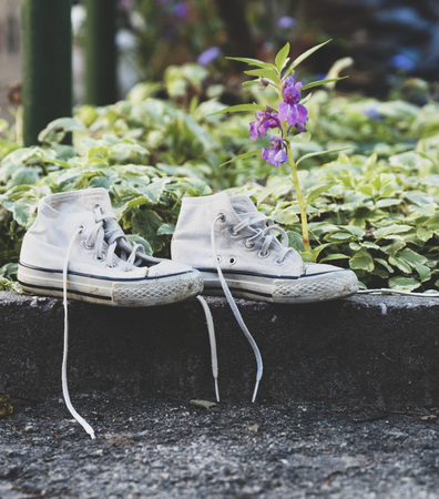 pair of old worn white textile sneakers with untied laces are on the curb, close upの写真素材