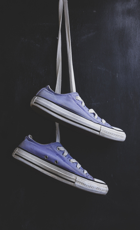 pair of purple textile sneakers hanging on a lace on a black background, vintage toningの写真素材