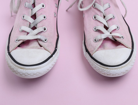 pair of old worn pink sneakers with white laces on a pink background, close upの写真素材