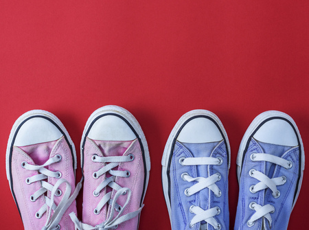 two pairs of worn textile sneakers with white laces on a red background, top view, copy spaceの写真素材