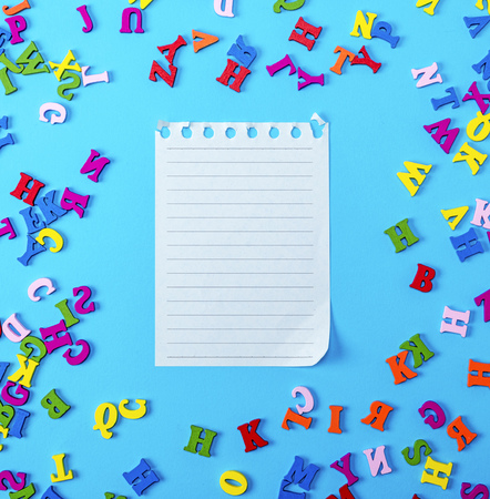 empty paper sheet in a line on a blue background surrounded by wooden multicolored lettersの写真素材