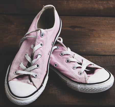 pair of old worn pink sneakers with white laces on a wooden background, vintage toningの写真素材