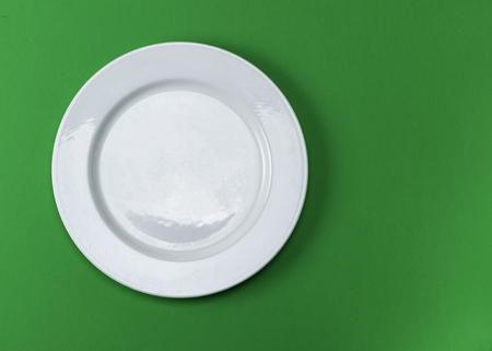 used white round plate with scratches on a green background, top view, copy spaceの写真素材