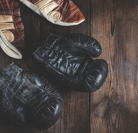 pair of very old leather black boxing gloves with laces and a pair of leather shoes on a brown...