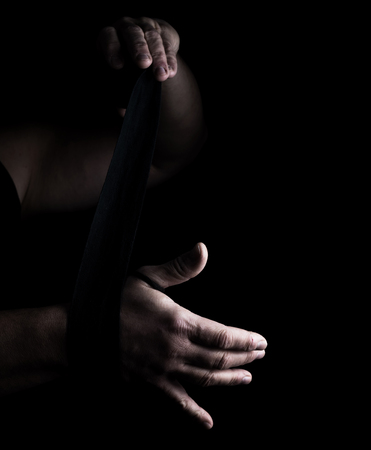 man wraps his hands in black textile bandage for sports, black backgroundの写真素材