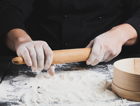 wooden rolling pin in men's hands, white wheat flour is poured on the table