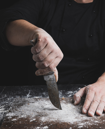 cook in black clothes holding a vintage old knife above the tableの写真素材