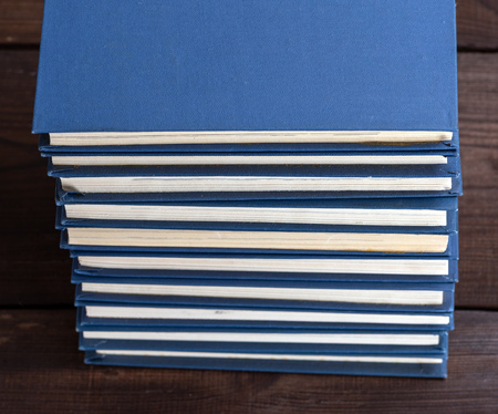 large stack of books in a blue cover on a brown wooden table, top viewの写真素材