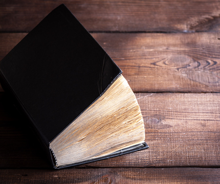 very old book with yellow pages and a black cover on a wooden surface, copy spaceの写真素材