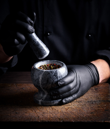 Chef in black latex gloves holds a stone mortar with a mixture of peppers, cooking and grinding spicesの写真素材