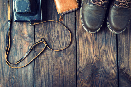 pair of leather brown shoes and an old vintage camera in a case on a wooden background, vintage toningの写真素材