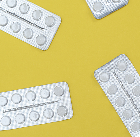 different white tablets in a package are scattered on a yellow background, top view