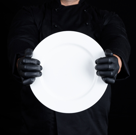 Chef in black uniform and black latex gloves holding a round empty plateの写真素材