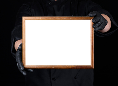 chef in black uniform and black latex gloves holding a wooden frame with white empty space, writing templateの写真素材
