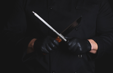 cook in black latex gloves sharpens a knife , vintage toning
