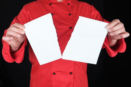 man in a red uniform holds a white sheet of paper torn in half, black backgroundの写真素材