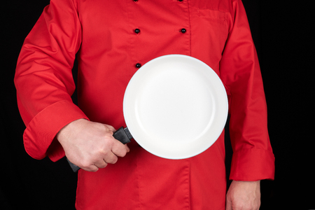 cook in red uniform holding an empty round white frying pan, black backgroundの写真素材