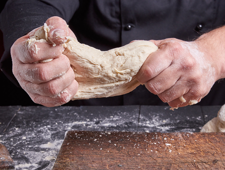 chef in black uniform kneads white wheat flour dough over the tableの写真素材