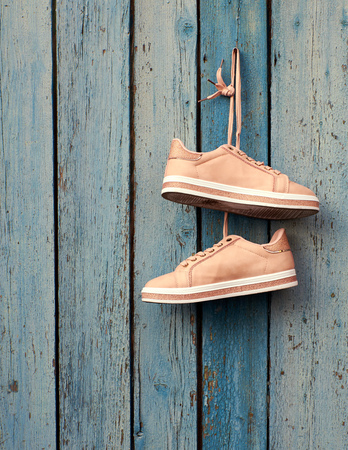 pair of beige female sports shoes hanging on a cord on a background of a blue old wooden wallの写真素材