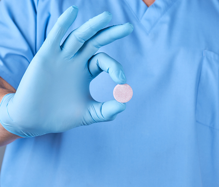 doctor in blue latex gloves holding a large round pill, male in uniformの写真素材