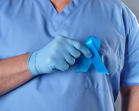 doctor in uniform and latex gloves holding a blue ribbon in his hand, a symbol of the fight and...