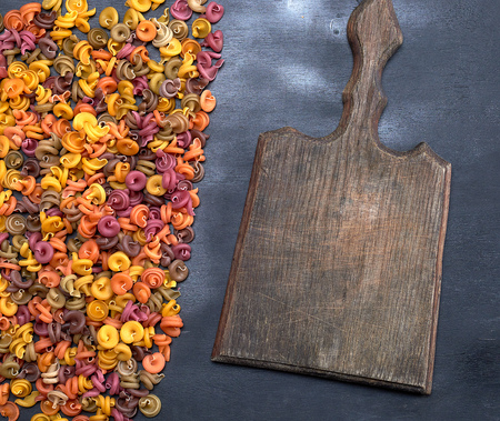 old empty wooden cutting board and unprepared fusilli pasta multicolored spiral of wheat flourの写真素材