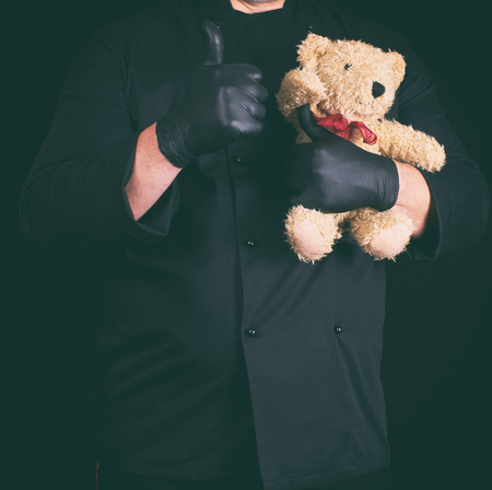 man in black clothes holding a brown teddy bear in his hands, black backgroundの写真素材