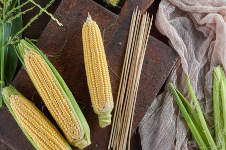 fresh ripe yellow corn cobs on a brown wooden board, top view