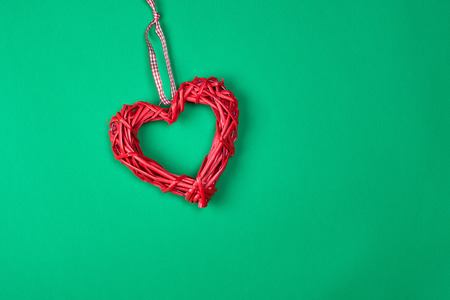 red decorative heart braided from a rod on a green background, copy space