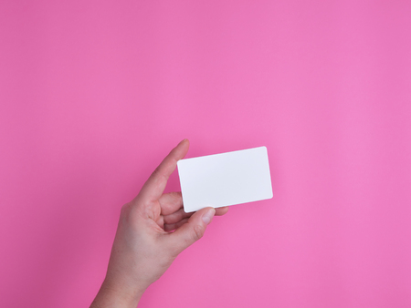 empty white rectangular business card in a female hand on a pink backgroundの写真素材