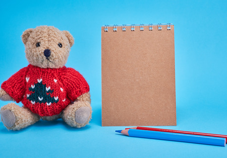 blank brown spiral notepad with brown pages, pencils and a little brown teddy bear on a blue backgroundの写真素材