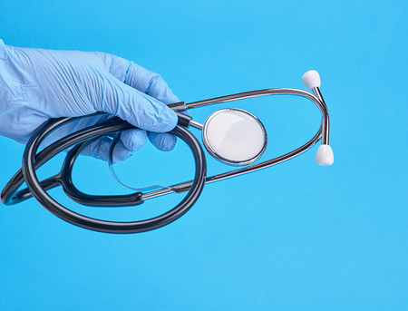 human hand in blue latex sterile gloves holding a medical stethoscopeの写真素材