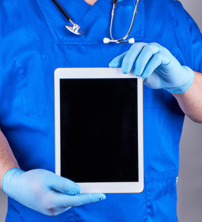 doctor in blue uniform and latex sterile gloves holding an electronic tablet with a blank black screen, gray backgroundの写真素材