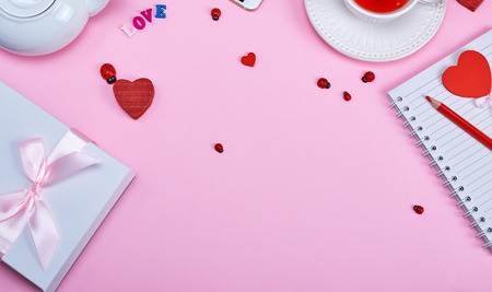 gift wrapped in a package  on a pink background, on the side a white cup of tea with berries of a viburnum and an open notebook in a lineの写真素材