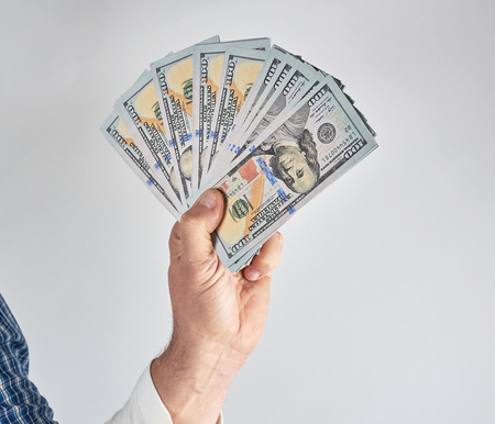 male hand holding a stack of one hundred dollar bills on a white backgroundの写真素材