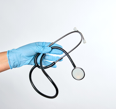 blue sterile gloved hand holding a black medical stethoscope on white background