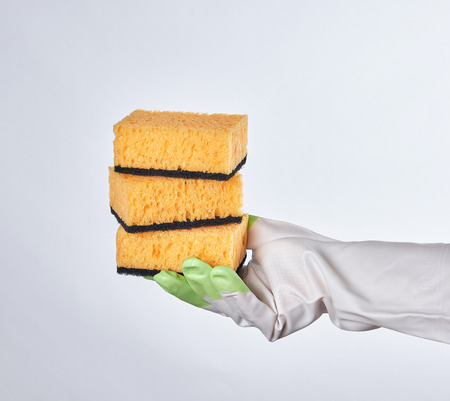 gloved hand holds yellow kitchen sponge, white backgroundの写真素材