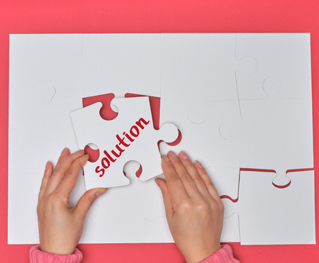 female hand holding white puzzle with the word solution, process of closing the missing element ,...