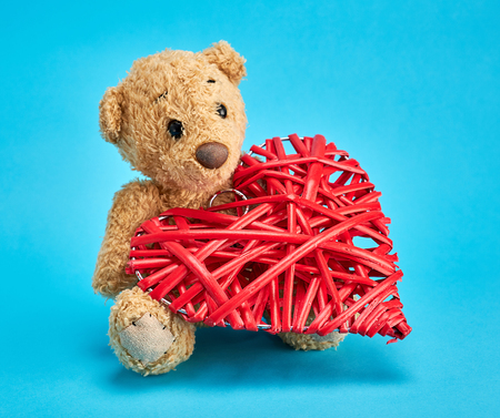 small teddy bear and a red decorative wicker heart on a blue backgroundの写真素材