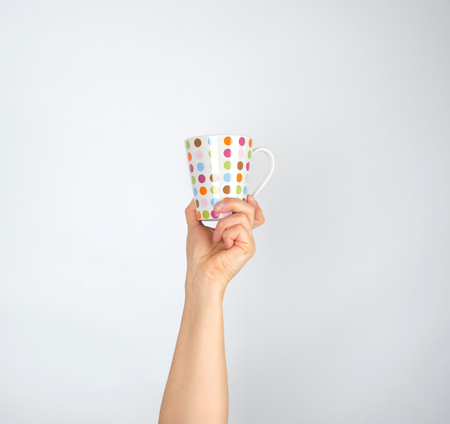 ceramic cup with multi-colored circles in a female hand on a white background,  hand is raised up