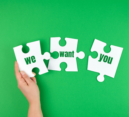 hand holding a white puzzle with the words we want you, green backgroundの写真素材