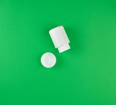 white plastic container for tablets, near the cover, green backgroundの写真素材
