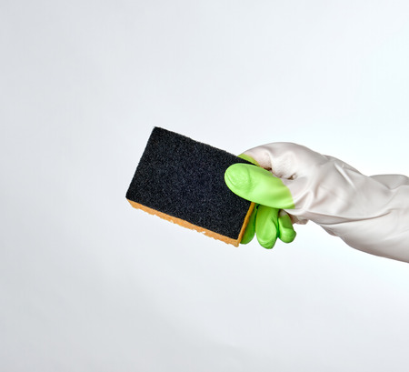gloved hand holds black kitchen sponge, white background