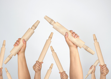 many hands raised up and holding kitchen wooden rolling pins on gray background, concept of riotの写真素材