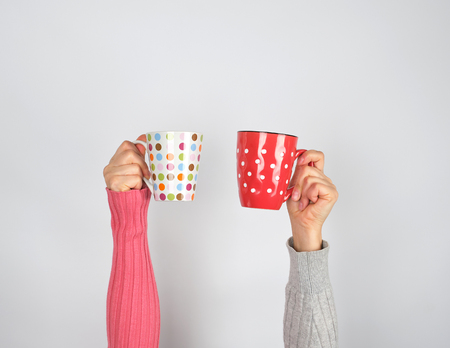 two hands in a sweater holding  ceramic mugs on a white backgroundの写真素材
