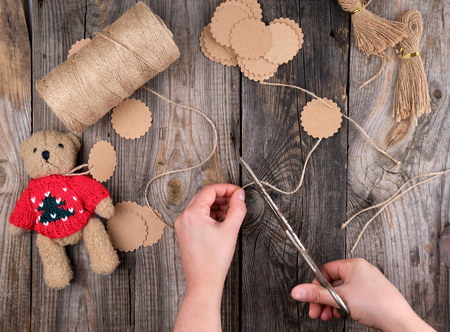female hands cut brown rope for tags, toy making process, gray wooden table