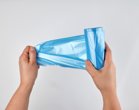 blue plastic trash bag in his hands on a white background, a man tears one from a roll