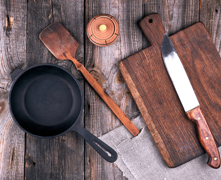 empty black round cast iron pan with handle, wooden cutting board and knife on a gray table, top viewの写真素材