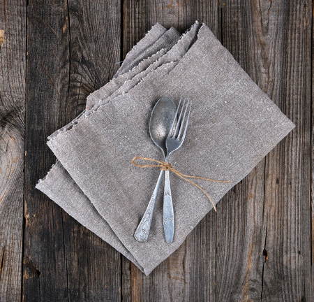 old metal fork and spoon tied with a brown rope on a gray linen napkin,  instruments are crossedの写真素材